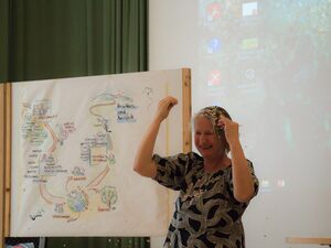 Frau mit viel Konfetti im Haar und auf ihrem grau-schwarzem kurzärmligen Oberteil. Die Frau freut sich und lacht.