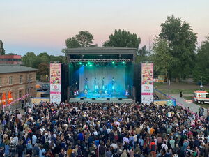 Eine große Bühne, rechts und links davon Banner vom Akzeptanzfestival. Vor der Bühne viele feiernde Menschen. Auf der Bühne eine Band.