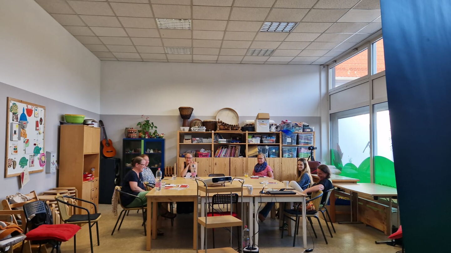 Ein großer Raum, große Tische die zusammen gerückt sind, darum sitzen 6 Frauen.