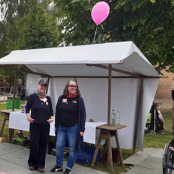 Zwei Frauen vor einem Aktionsstand. Neben dem Stand zwei Rollstühle.