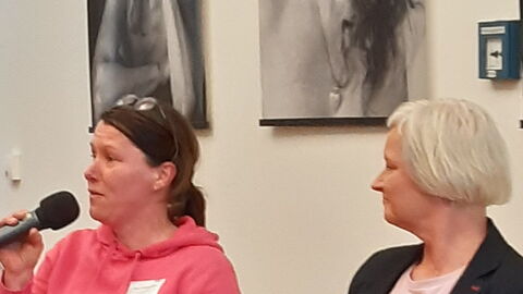 Diskussionsrunde. Drei Frauen sitzen nebeneinander. Frau im pinken Pulli spricht in ein Mikro.