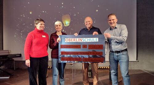 Vier Personen halten eine großen Scheck von der Oberlinschule in der Hand. Von links, 2 Frauen und 2 Männer. Sie stehen in einem großen Raum.