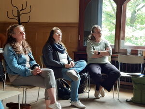 Drei Frauen sitzen auf Stühlen in einem Raum.
