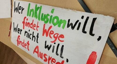 Großes Plakat auf dem Tisch. Text: "Wer Inklusion will, findet Wege. Wer nicht will, findet Ausreden!"