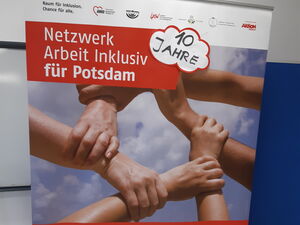 Das große Roll-Up-Banner vom Netzwerk Arbeit inklusiv mit einer kleinen Wolke die angeklebt wurde. In der Wolke steht: 10 Jahre