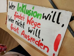 Großes Plakat auf dem Tisch. Text: "Wer Inklusion will, findet Wege. Wer nicht will, findet Ausreden!"