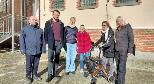 Gruppenfoto, 2 Männer und vier Frauen stehen im Innenhof eines Gefängnis. Vergitterte Fenster.