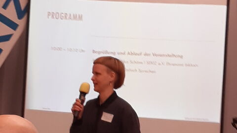 Frau mit kurzen blonden Haaren mit Mikrofon stellt das Programm vor.