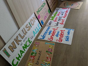 Protest-Plakate auf dem Boden und an die Wand gelehnt. Mit Sprüchen wie : Demokratie braucht Inklusion.