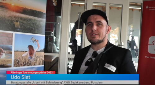 TV Ausschnitt. Interview. Ein junger Mann mit Basecap, weißes T-Shirt, schwarze Anzugjacke. In einem Raum mit Glastüren.