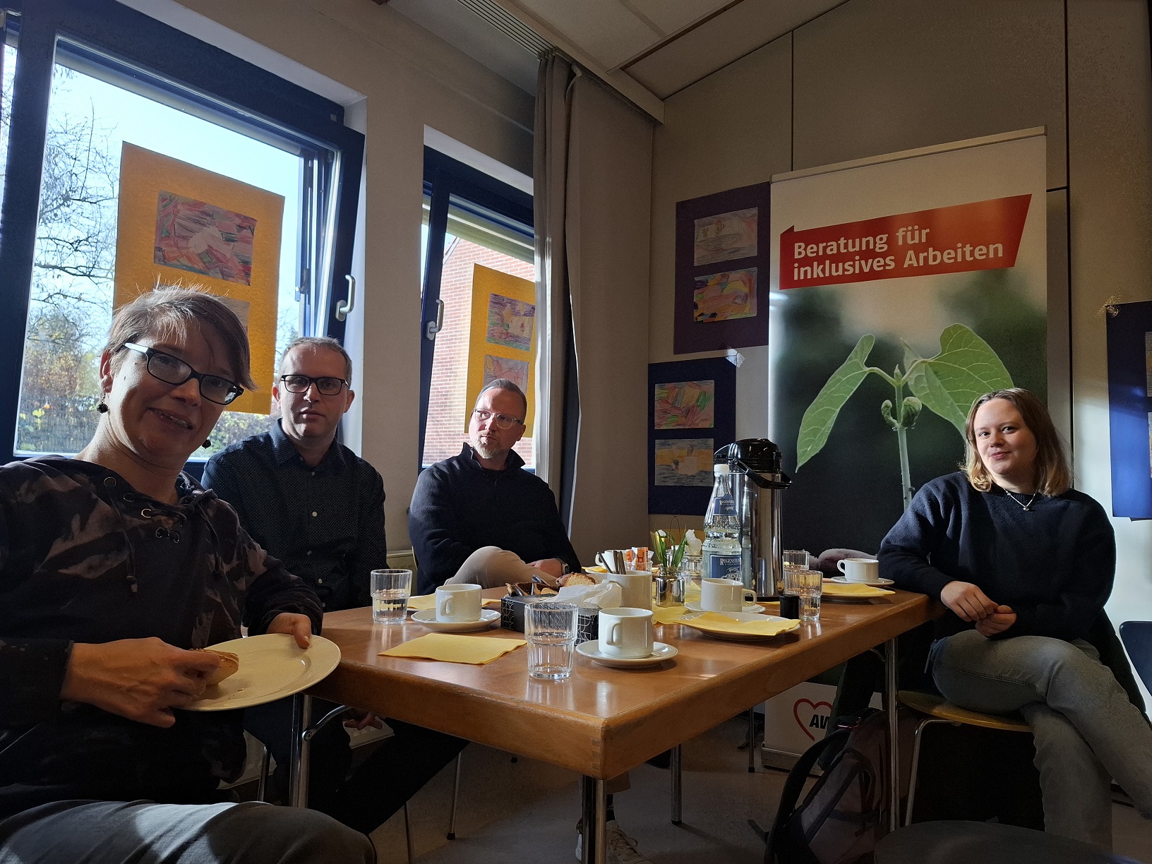 4 Personen an einem Tisch mit Kaffee und Kuchen. 2 Frauen und 2 Männer.