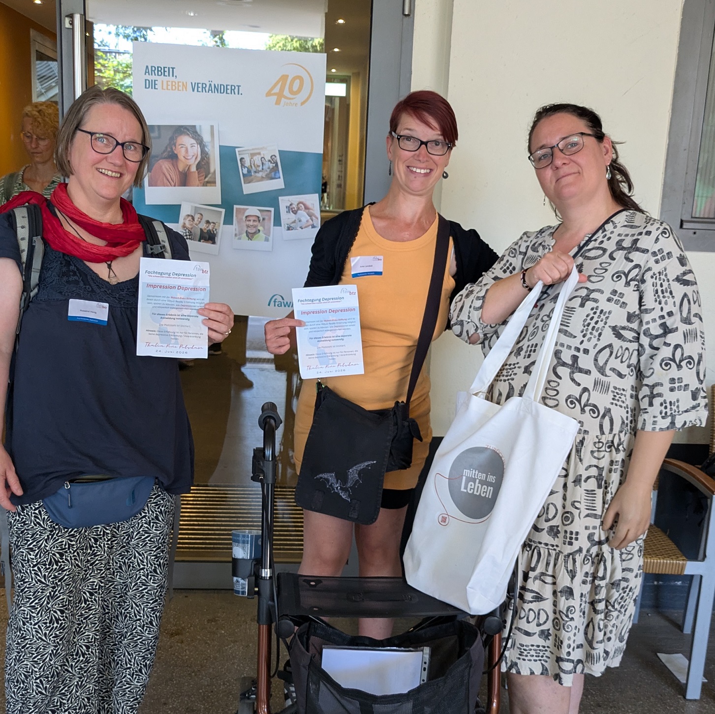 Teamfoto: 3 Frauen vor einem Eingang. alle sommerlich gekleidet. 2 halten das Programm der Tagung in die Kamera.